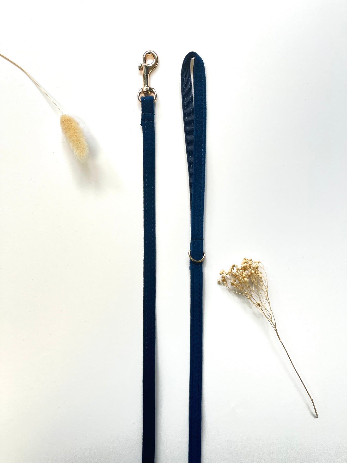 Laisse pour chien bleu marine Chevron, avec mousqueton et collier réglable, posée à côté d’un brin de plante sèche.