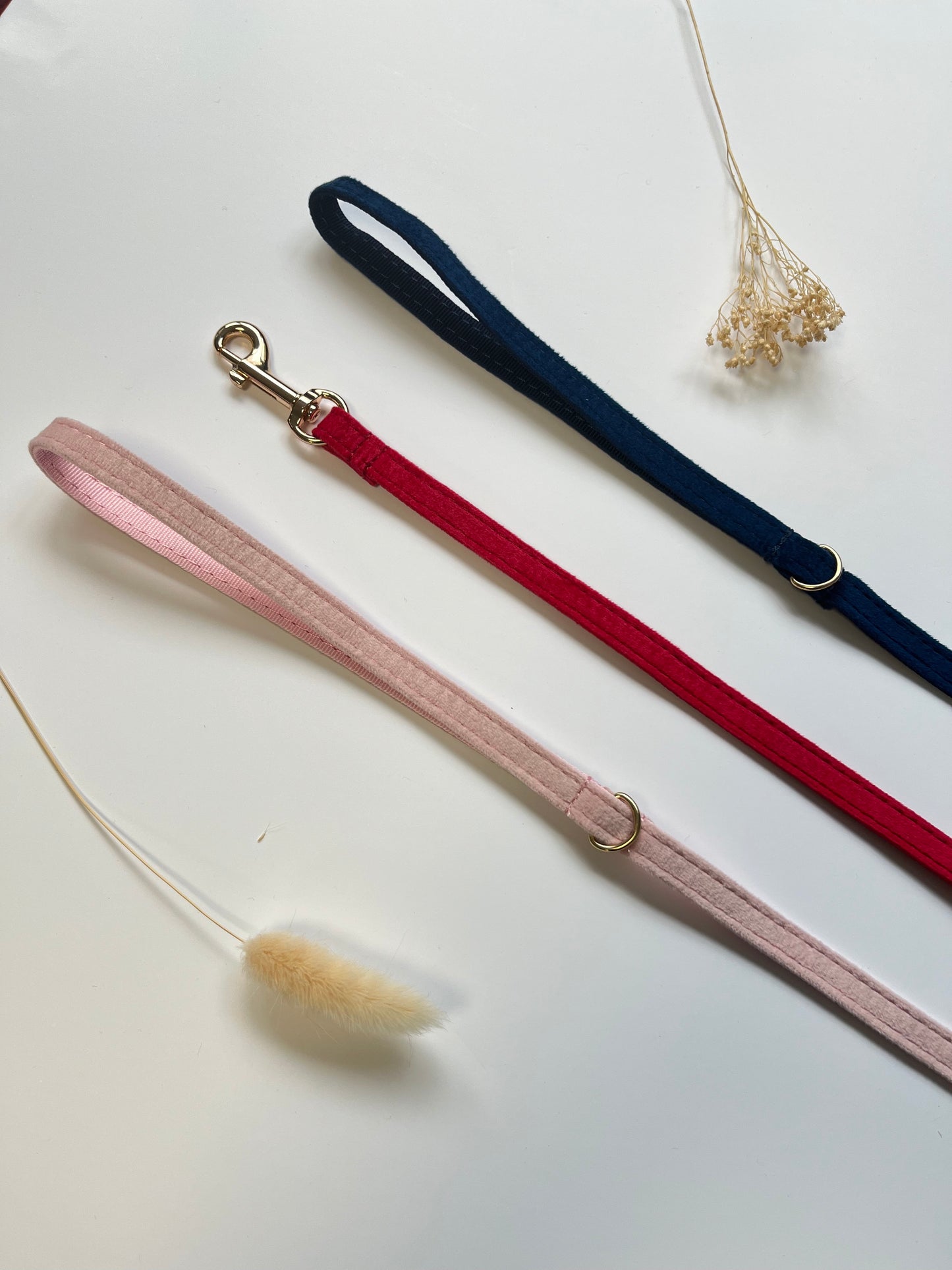 Laisse chat velours lisse rose avec mousqueton métallique et rosé, posé sur surface claire.