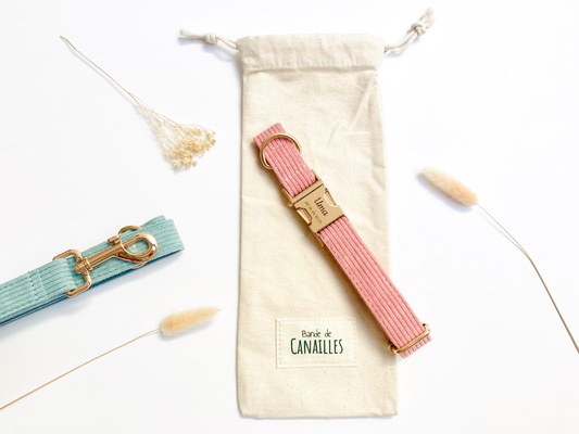 Pochette cadeau en tissu beige avec une bandoulière rose et des attaches dorées, décor minimaliste.