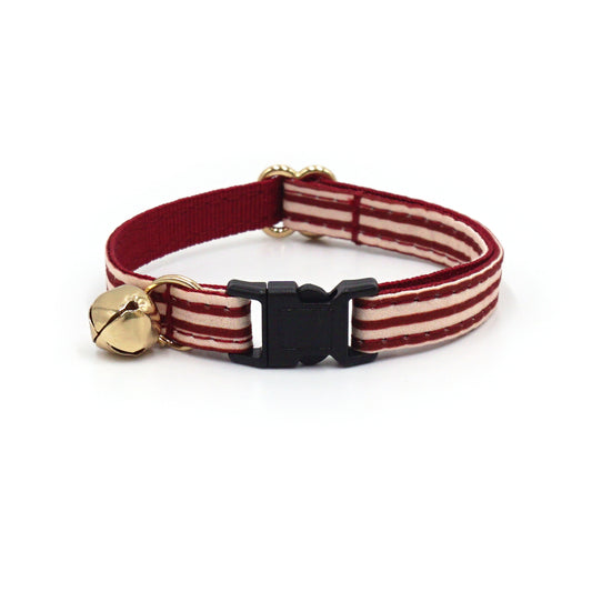 Collier chat anti-étranglement en coton rayé Bordeaux avec boucle noire et petit charme cloche doré.